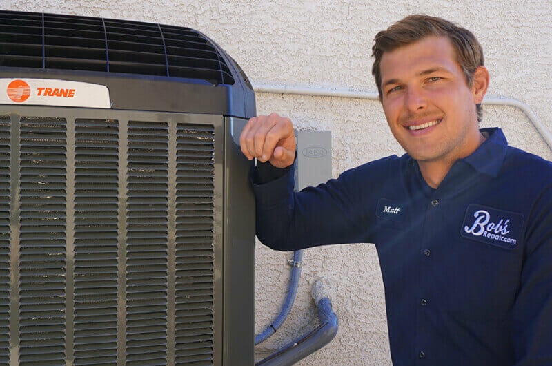 A cheerful Bob's Repair technician, in professional uniform, standing next to an AC unit, ready to provide top-notch repair services in Las Vegas