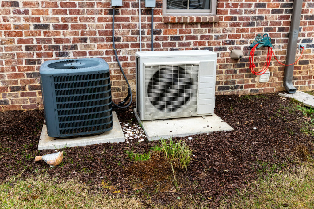 Two outdoor AC condenser units mounted side by side against a brick exterior wall