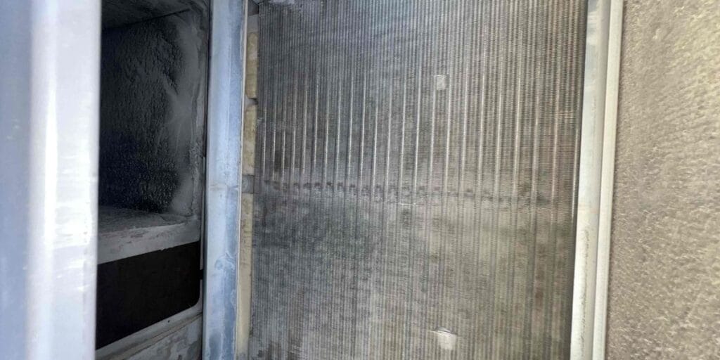 The interior of an AC housing shows white frost coating one side of the metal, next to a coil bank covered in dust on the other side.