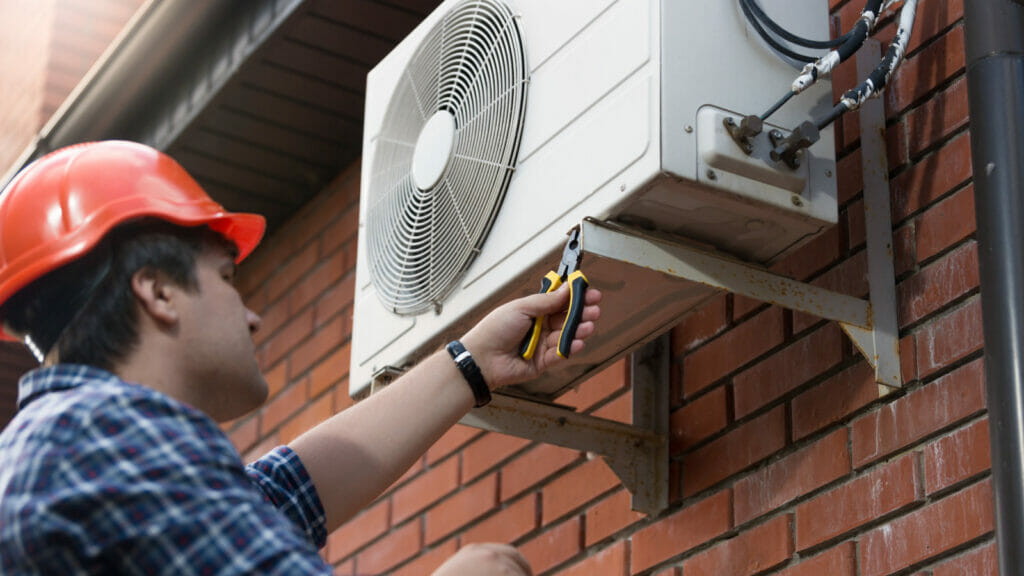 A person working to strategically position an outdoor AC unit in the shade, symbolizing the focus of the article on the potential benefits of shading your AC unit.
