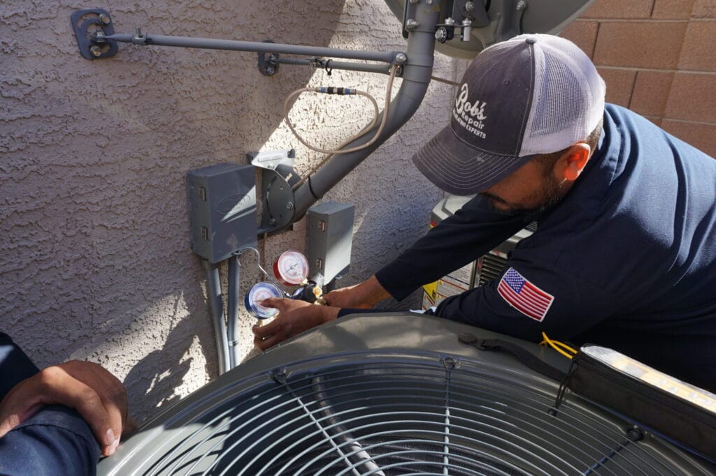 HVAC technician checking refrigerant levels with gauges on an outdoor air conditioning unit.