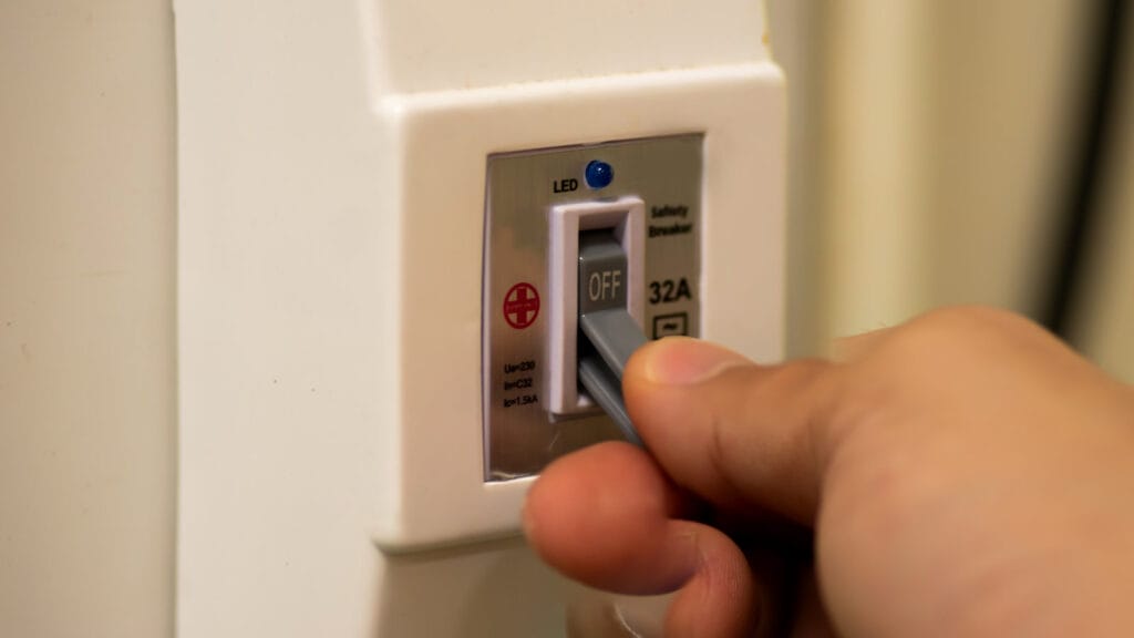Close-up of a hand switching an AC circuit breaker to the 'Off' position, indicating a safety measure for air conditioner electrical issues.