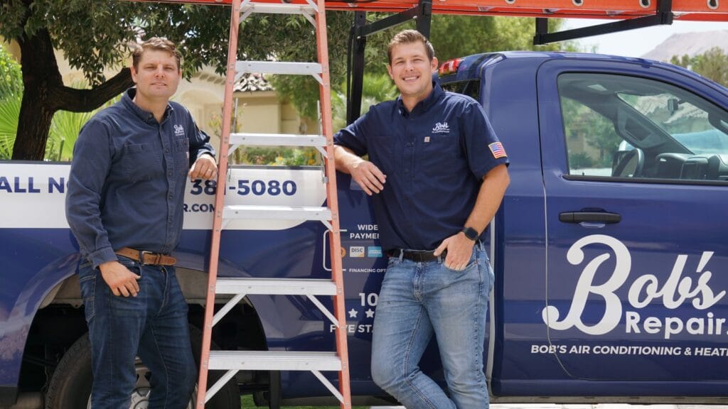 Two smiling technicians from Bob's Repair, wearing company uniforms, stand ready beside their service vehicle and ladder, suggesting preparation for an air duct cleaning appointment at a home.