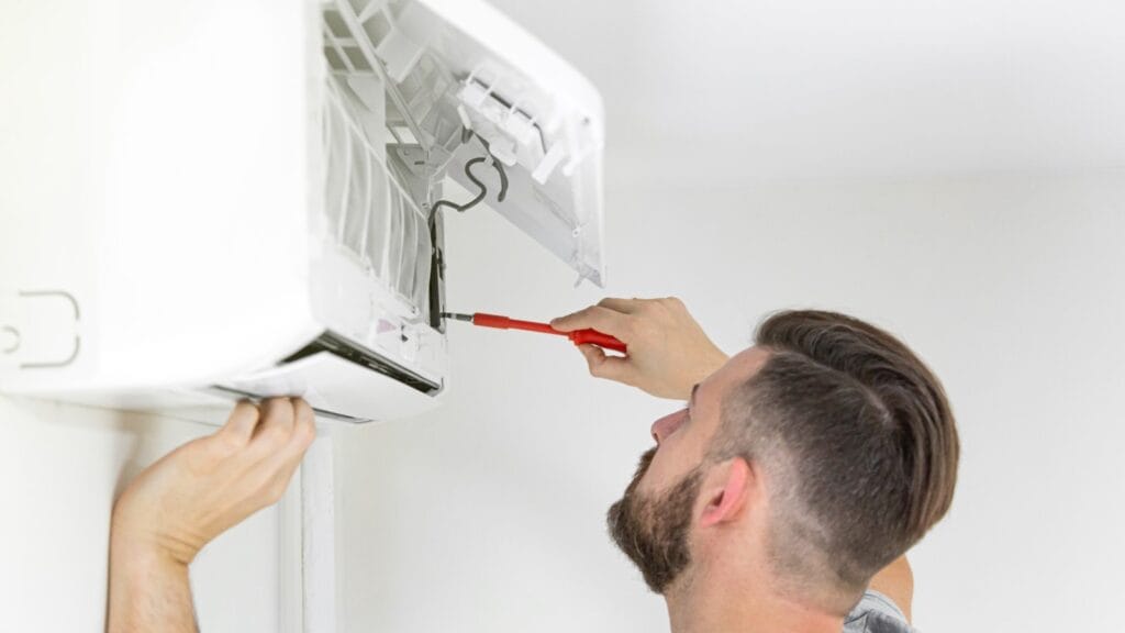 Focused maintenance action as a person troubleshoots an air conditioner.. They use a red screwdriver to adjust the internals of a white wall-mounted AC unit. The open front panel reveals the complex components inside, indicative of common issues homeowners can learn to fix themselves, promoting self-reliance and cost-saving on repairs