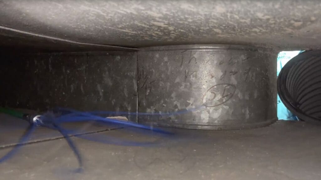Close-up view of a dusty and dirty air duct interior, with visible debris accumulation and a partial view of a flex duct, highlighting the need for regular cleaning to maintain indoor air quality for a healthier home environment.