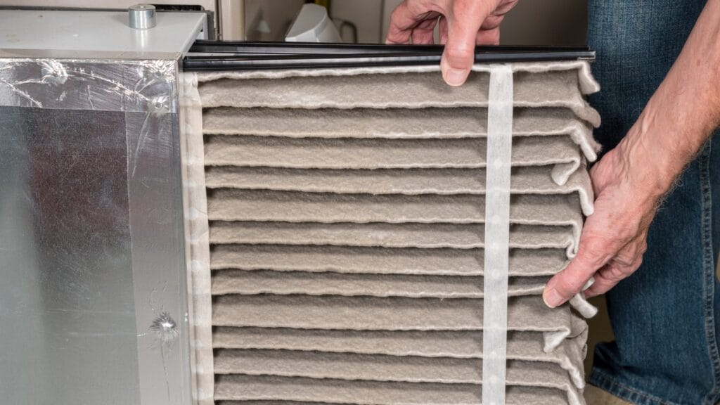 A person removing a dirty HVAC air filter from a home furnace, highlighting the importance of regular maintenance for indoor air quality.