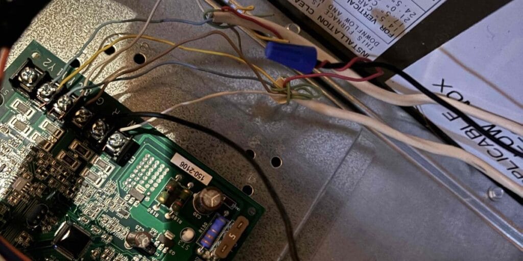 A green circuit board with several wires attached sits inside an open metal control panel