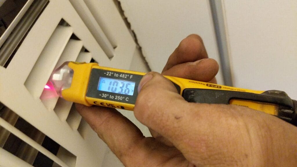 Technician using an infrared thermometer to measure heated air temperature at a supply vent, ensuring the furnace is operating at the correct outpu