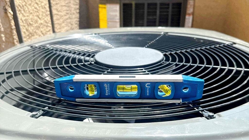 Level tool placed on top of an outdoor central air unit to verify even installation.