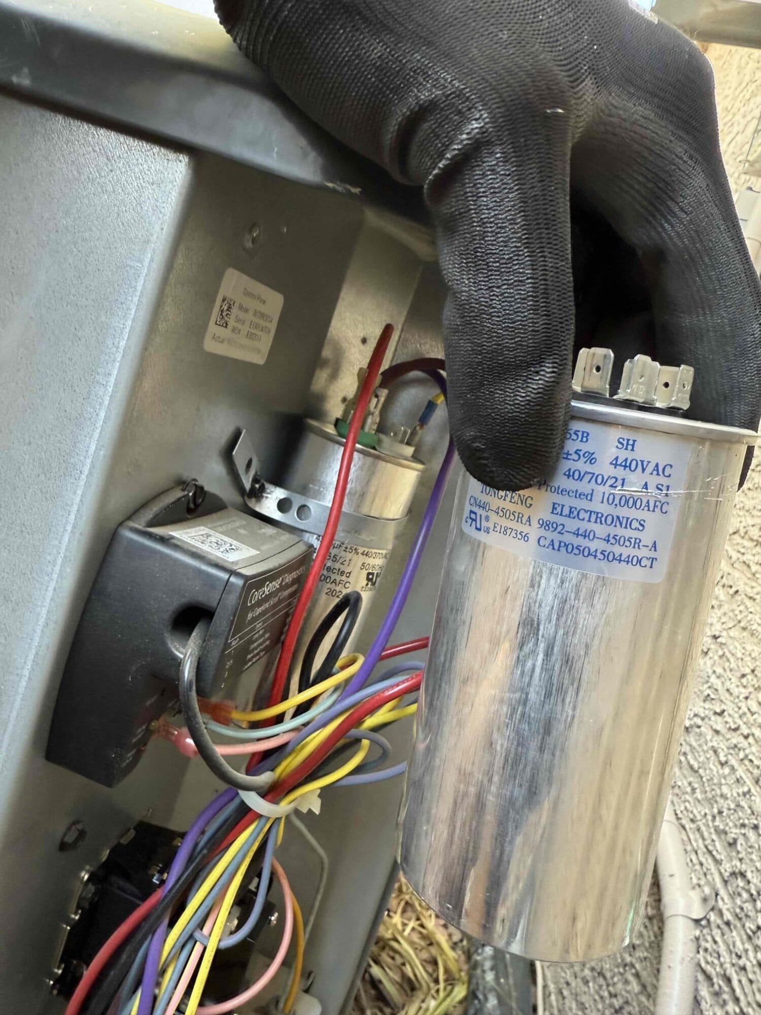 Technician holding a failed dual-run capacitor inside the condenser unit.