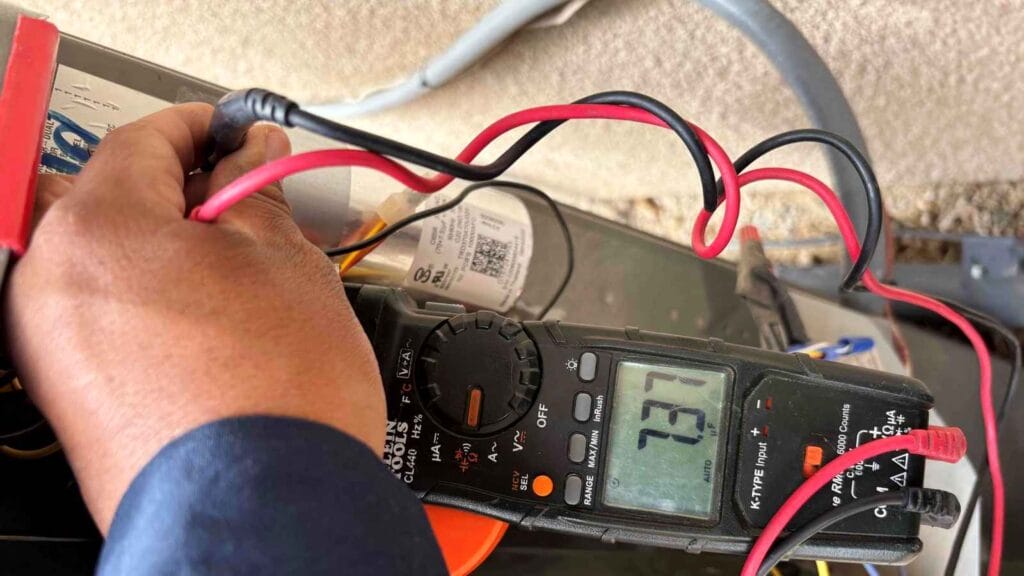 Technician using a clamp meter to test an electrical component, like an AC capacitor, during a detailed air conditioner maintenance service.