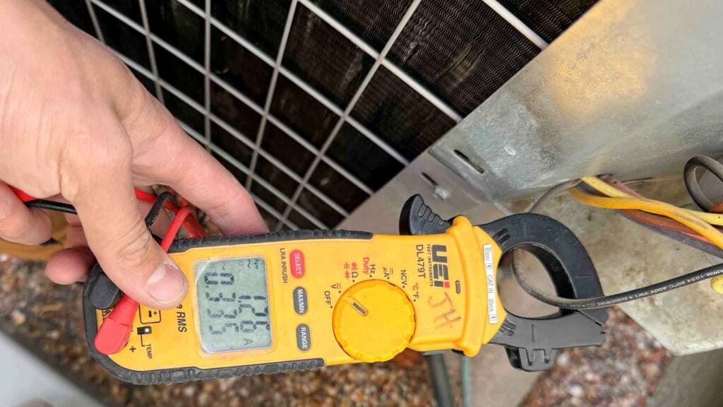 HVAC professional checking electrical current on an outdoor AC unit with a clamp meter as part of routine air conditioner maintenance