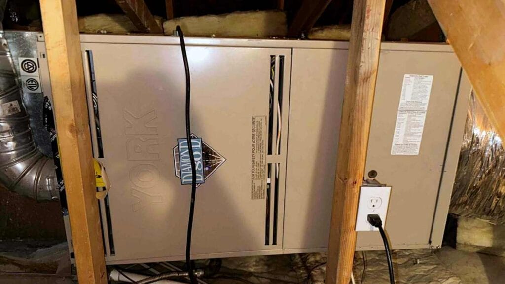 A York Diamond 80 furnace installed within a wooden attic frame with visible wiring and insulation, illustrating a standard residential heating system that may need upgrading to high-efficiency models.