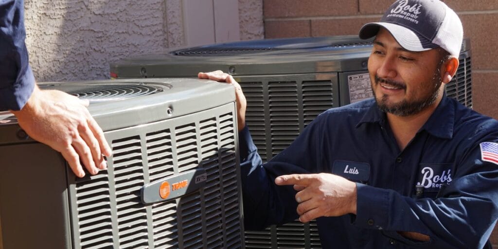 Technician Luis smiles and points toward a Trane condenser next to a second outdoor unit