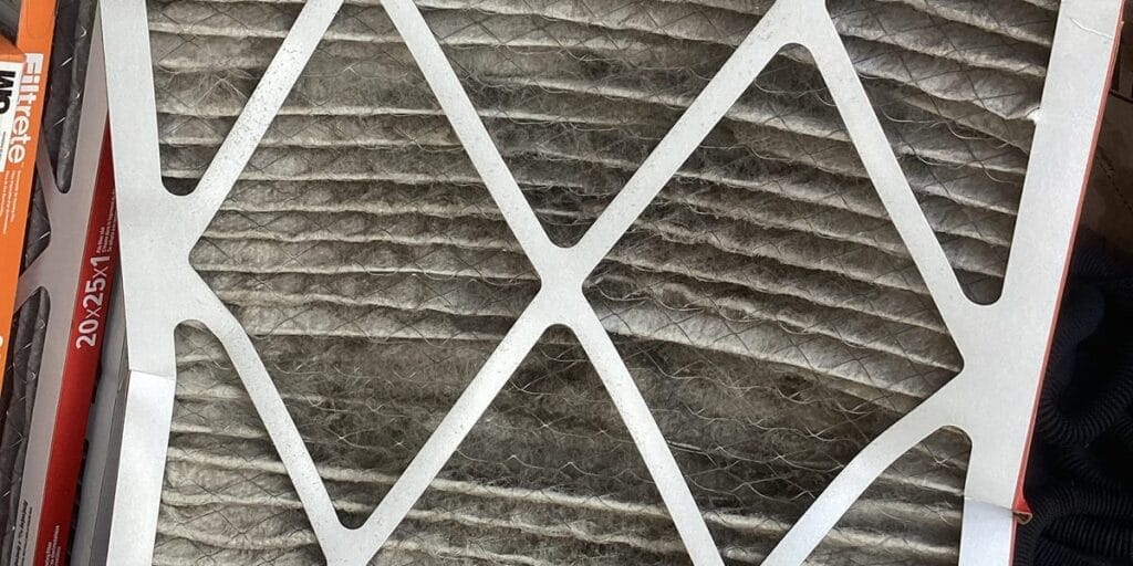 A pleated air filter caked in a thick layer of grey dust sits next to unopened replacement filters.