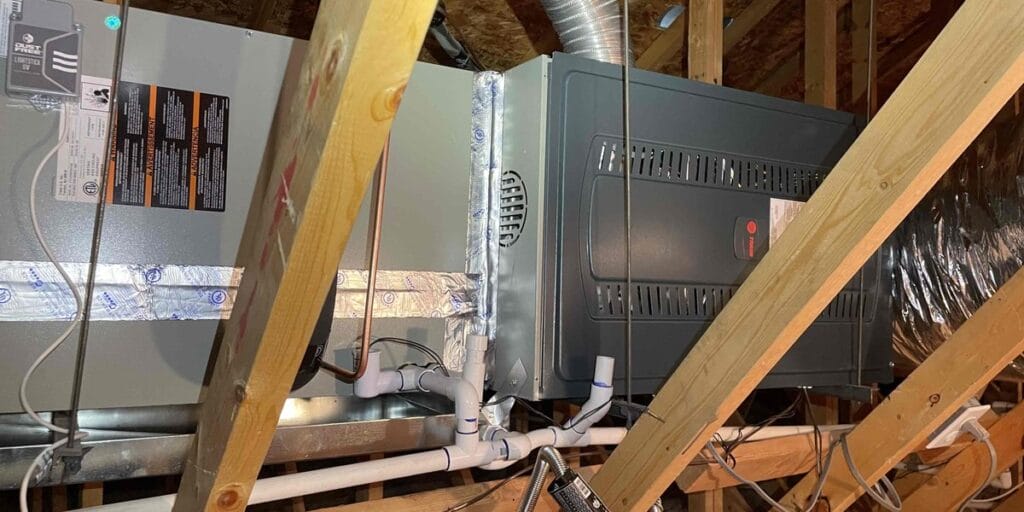 An attic furnace and air handler system surrounded by flex ductwork, insulation, and roof framing.
