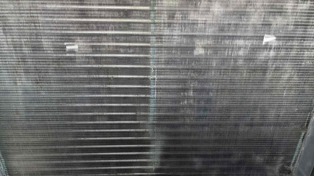 Close up of an evaporator coil with fins showing patches of dark residue and mineral streaking.