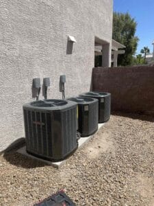 Three Trane condenser units sit side by side along a stucco wall in a gravel side yard, built to keep a home cooled through an AC electric power outage in neighborhoods like Summerlin and Henderson.
