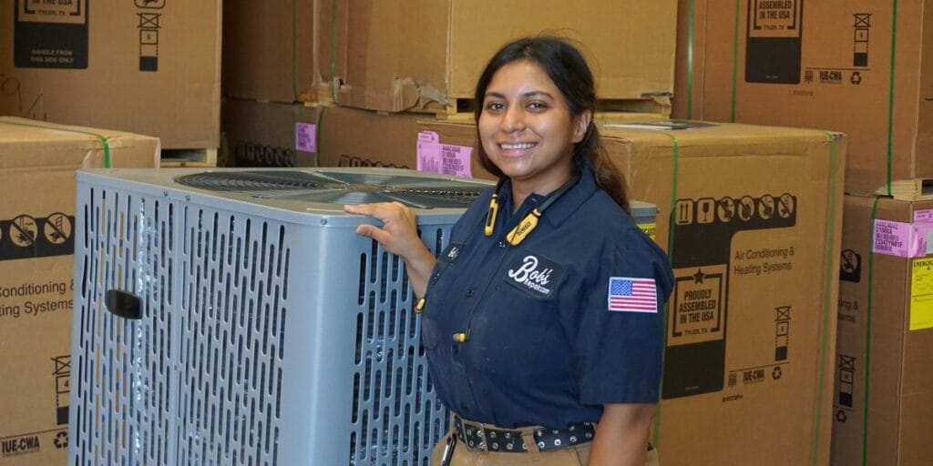 A Bob's Repair technician in uniform stands beside a new packaged outdoor air conditioning unit in a stocked warehouse.