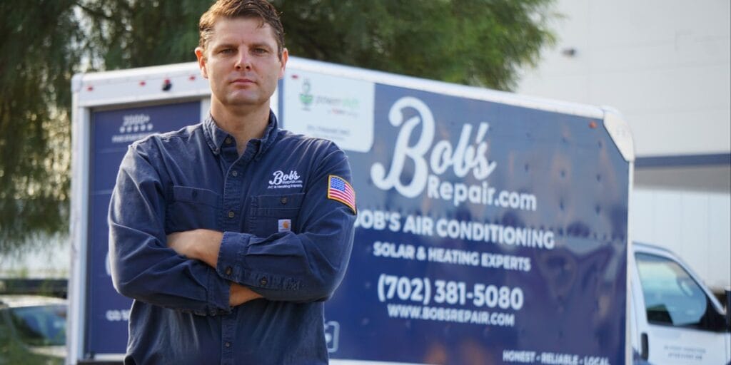 A Bob's Repair technician stands with his arms crossed in front of a company branded service truck advertising air conditioning, solar, and heating services.