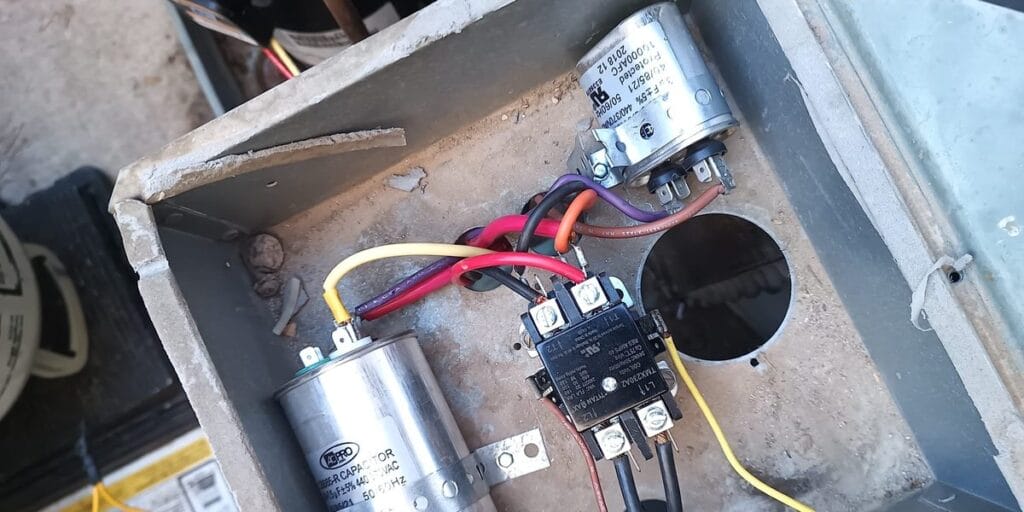 Inside an outdoor unit's electrical compartment, showing a run capacitor, a contactor, and colored wires connected between them.
