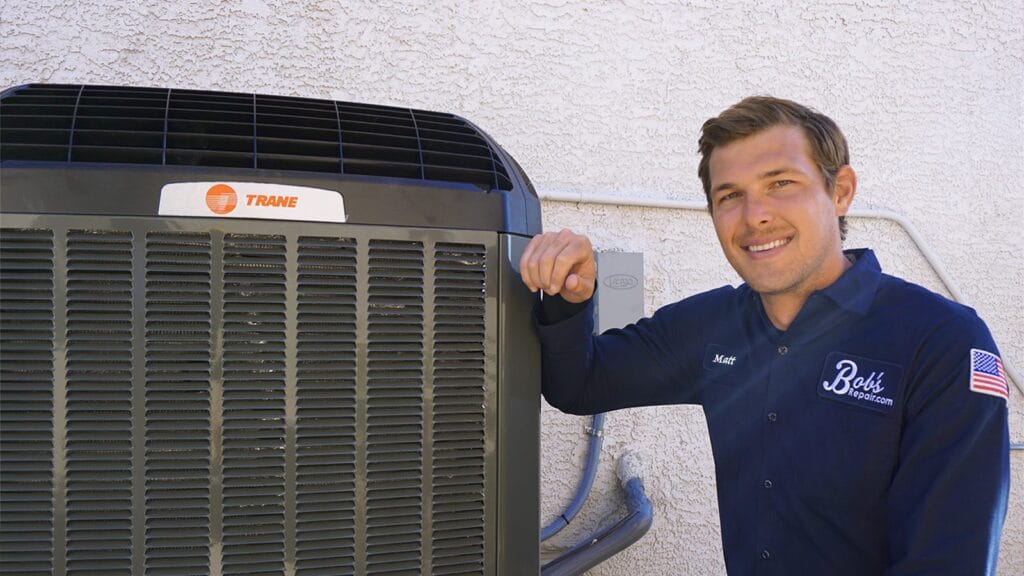 A Bob's Repair technician named Matt rests his hand on an outdoor Trane AC unit and smiles at the camera outside a stucco home.