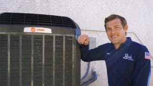 A Bob's Repair technician named Matt rests his hand on an outdoor Trane AC unit and smiles at the camera outside a stucco home.