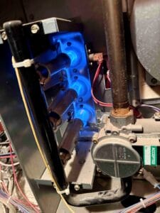 Inside view of a gas furnace showing three bright blue flames burning cleanly inside the metal burner tubes right next to a gas valve and some wiring.