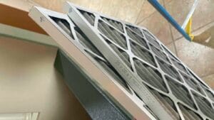 Two gray pleated air filters lean against each other at an angle, with their white cardboard frames and printed size label facing the camera.