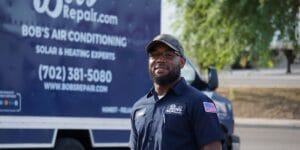 A professional HVAC technician from Bob's Repair wearing a navy blue uniform and cap stands in front of a company service truck.