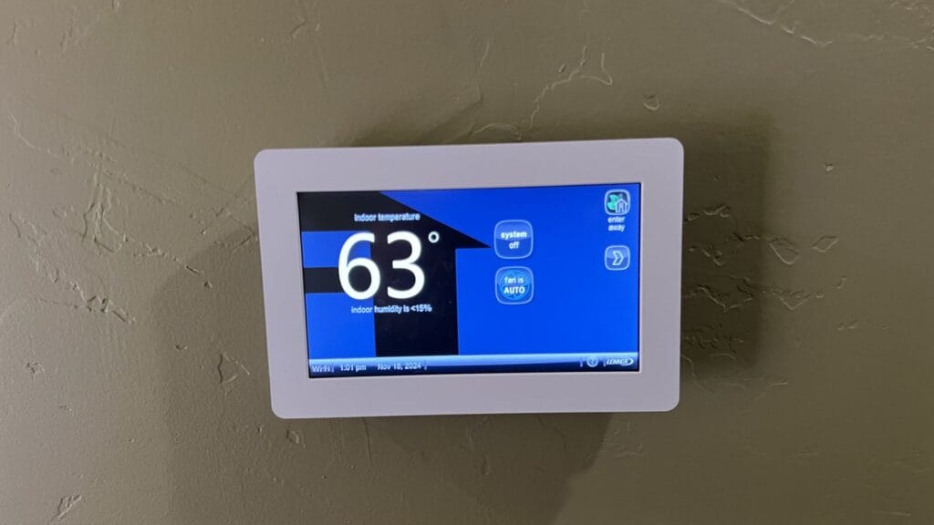 Wall thermostat with a blue screen showing an indoor temperature of 63 degrees