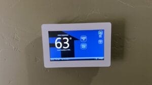 Wall thermostat with a blue screen showing an indoor temperature of 63 degrees