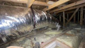Silver insulated flexible air duct stretching across wood rafters and pink insulation in a Las Vegas attic